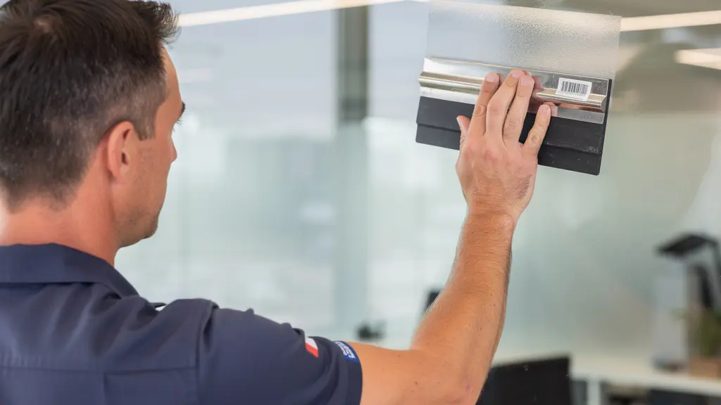 Technicien posant un film anti-chaleur sur une grande vitre avec raclette professionnelle