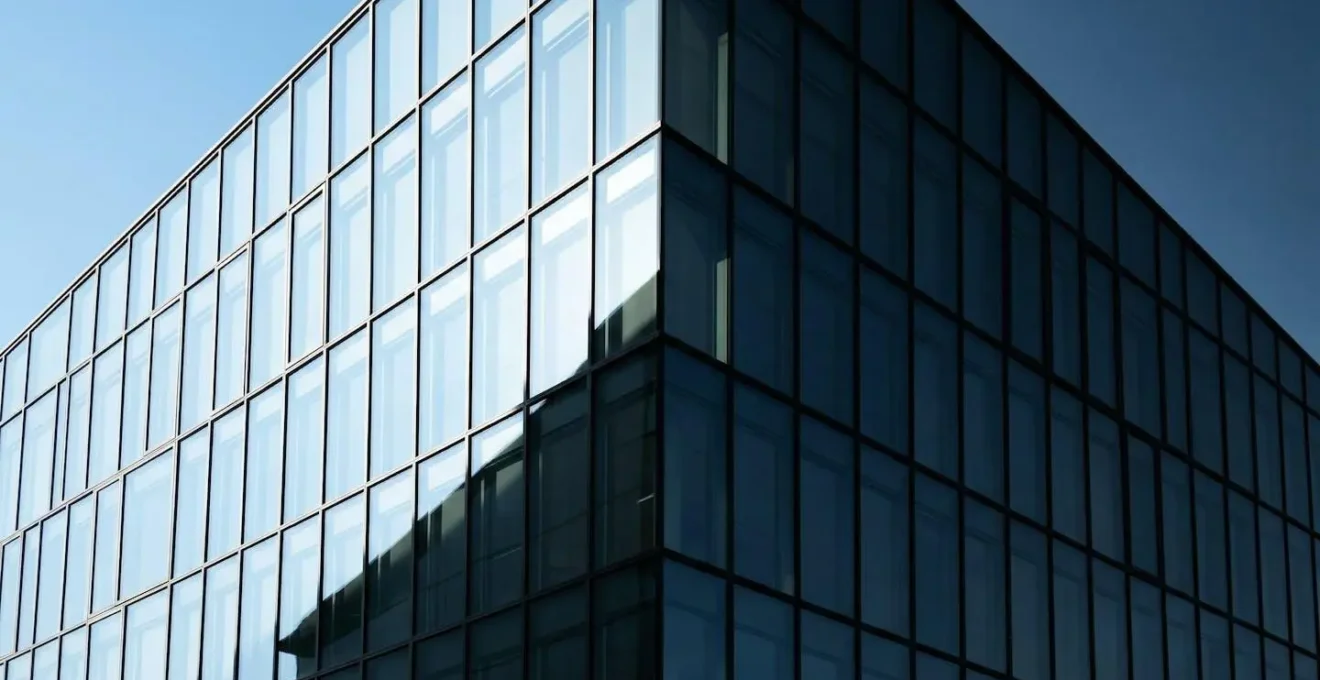 Façade vitrée avec contraste dramatique entre zones ensoleillées et ombragées montrant le stress thermique